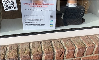 Schaufenster Stadt Coiffeur Meppen mit schlecht frisiertem Puppenkopf, der auf die Thematik Häusliche Gewalt hinweist. Slogan: 