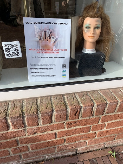 Schaufenster Stadt Coiffeur Meppen mit schlecht frisiertem Puppenkopf, der auf die Thematik Häusliche Gewalt hinweist. Slogan: "Häusliche Gewalt lässt sich nie schön stylen" © Stadt Meppen